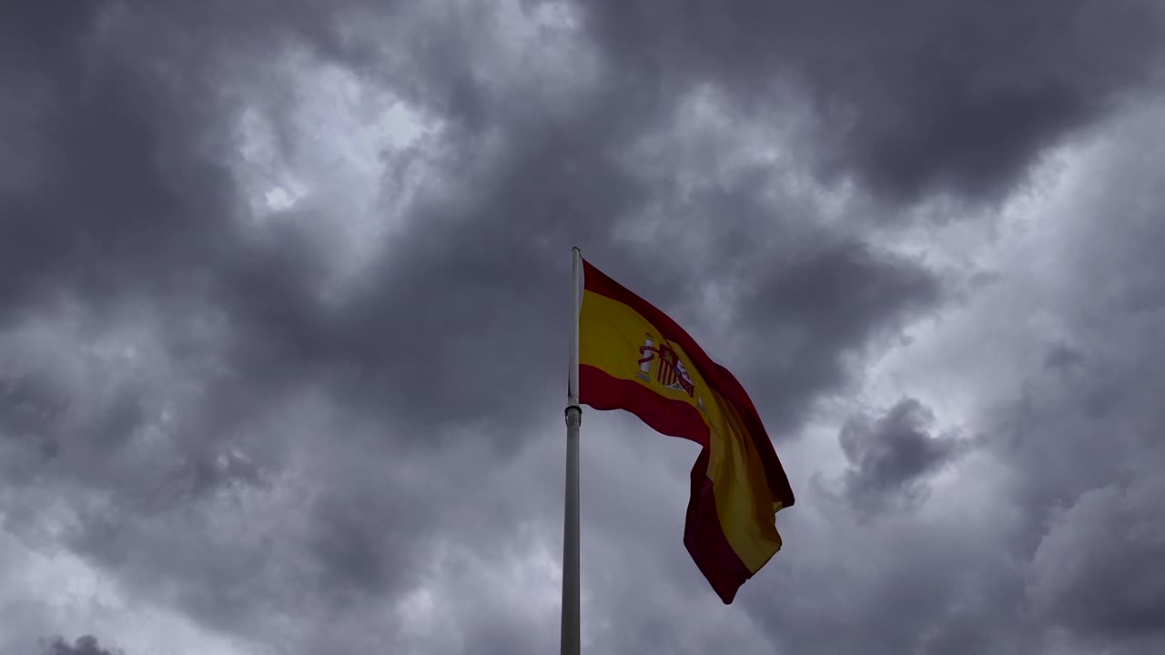 Bandiera nazionale spagnola, vista dal basso, sotto un cielo tempestoso, drammatico e mutevole