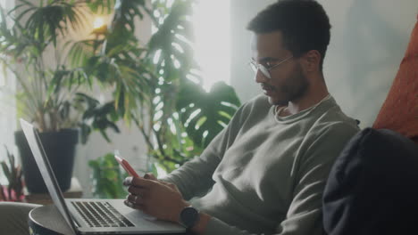 man using smartphone and laptop on sofa