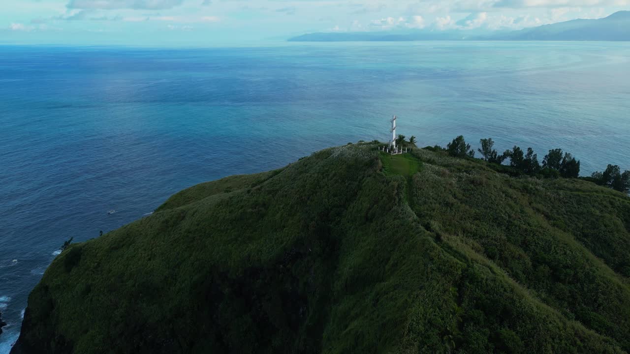 Closing‑in aerial of Dingalan Lighthouse in Aurora, approaching the white tower perched on the green cliffside, with the vast blue sea stretching into the horizon