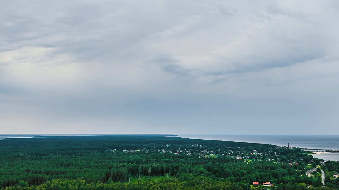 Dramatic cloudy sky over lush green landscape with forest and distant open field, storm crossing landscape