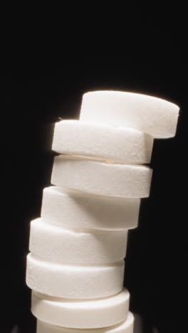 curved stack of white round pills spins shaking ready to collapse on black background. production of effective medication for health treatment macro