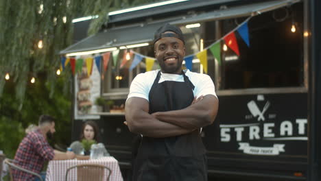 Portrait-Of-Joyful-Young-Man-In-Apron-Smiling-To-Camera-At-Food-Court-Outdoors-On-Sunny-Warm-Day