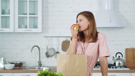 the girl in the kitchen takes out an orange and an apple from a paper bag. vegetarian food