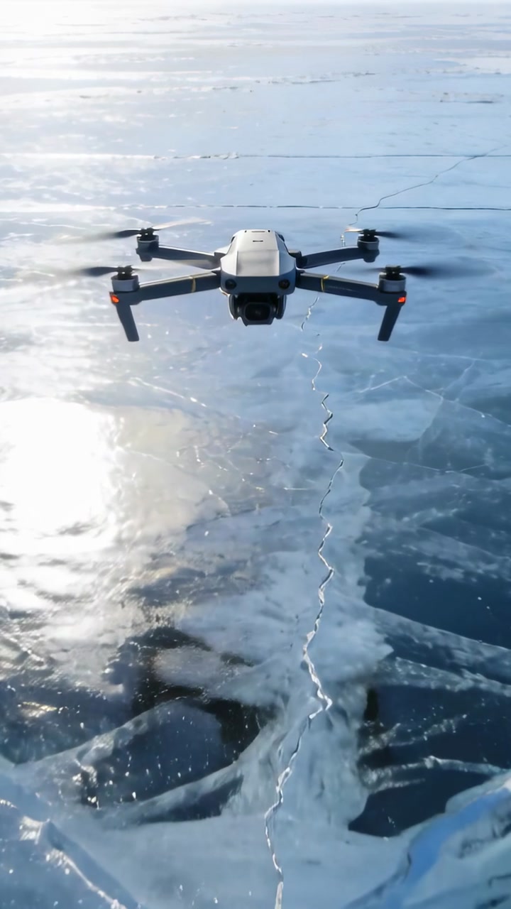Vertical video: Hovering quadcopter holding frontal camera over frozen lake, showing ice fissures