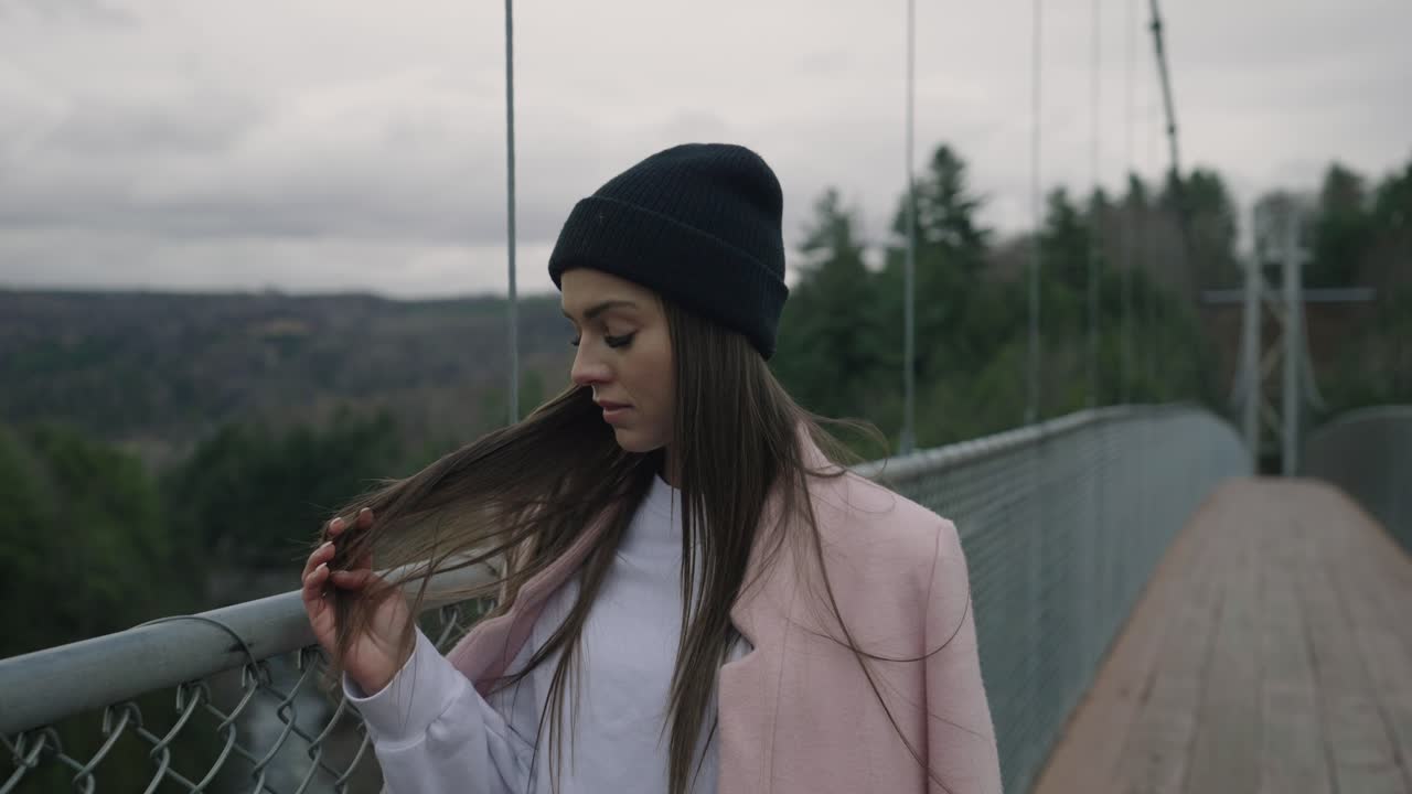 Attraktiv kvinde, der stryger sit lange hår, mens hun går på broen om vinteren i Coaticook, Quebec, Canada. Slowmotion-optagelse