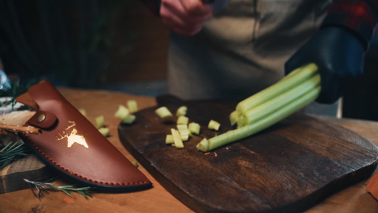 A person cutting fresh celery on a rustic wooden board in a cozy kitchen setup
