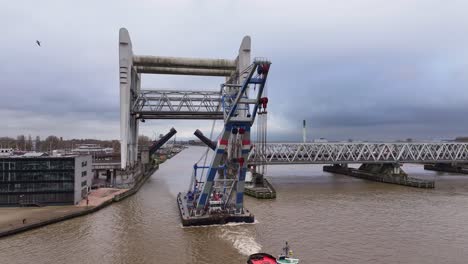 industrial crane floats through railway bridge tugged by small vessel