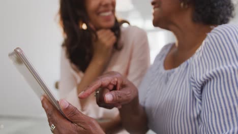 Senior-mixed-race-woman-using-a-digital-tablet-with-her-daughter,-in-social-distancing-