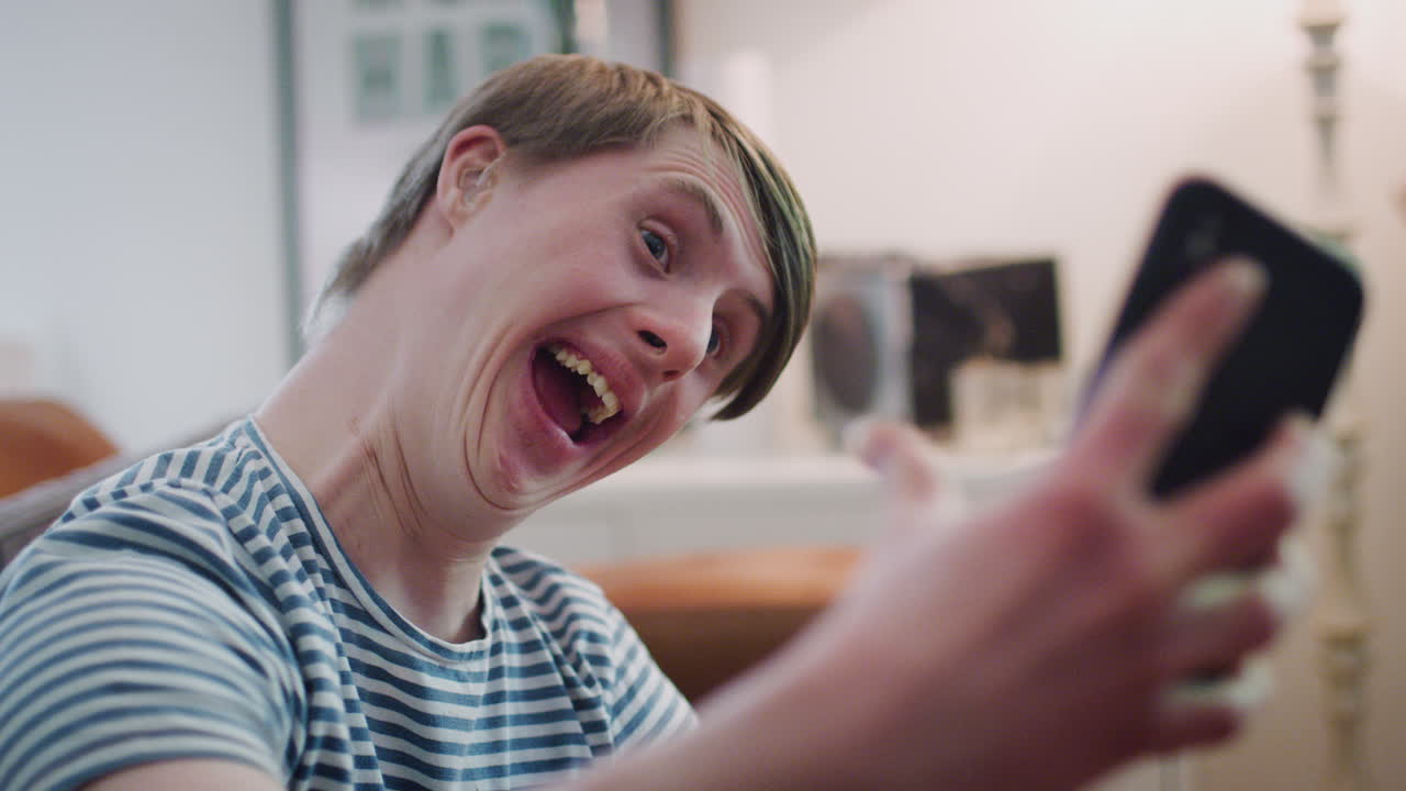 hombre con síndrome de down sentado en el sofá usando un teléfono móvil para tomarse una selfie en casa