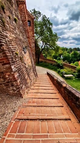 pov descending on brick pathway and near walls of trausnitz castle surrounded by green trees
