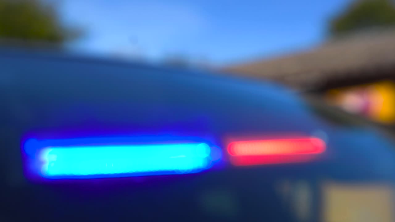 Abstracted day time red and blue police LED law and order flashing lights blurred and in a vehicle car windshield flashing. Blue sky and green nature seen in the bokeh blurry background also