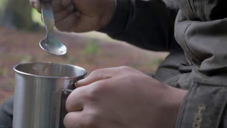 Male-eating-from-a-metal-cup-in-the-forest,-Static-Close-up