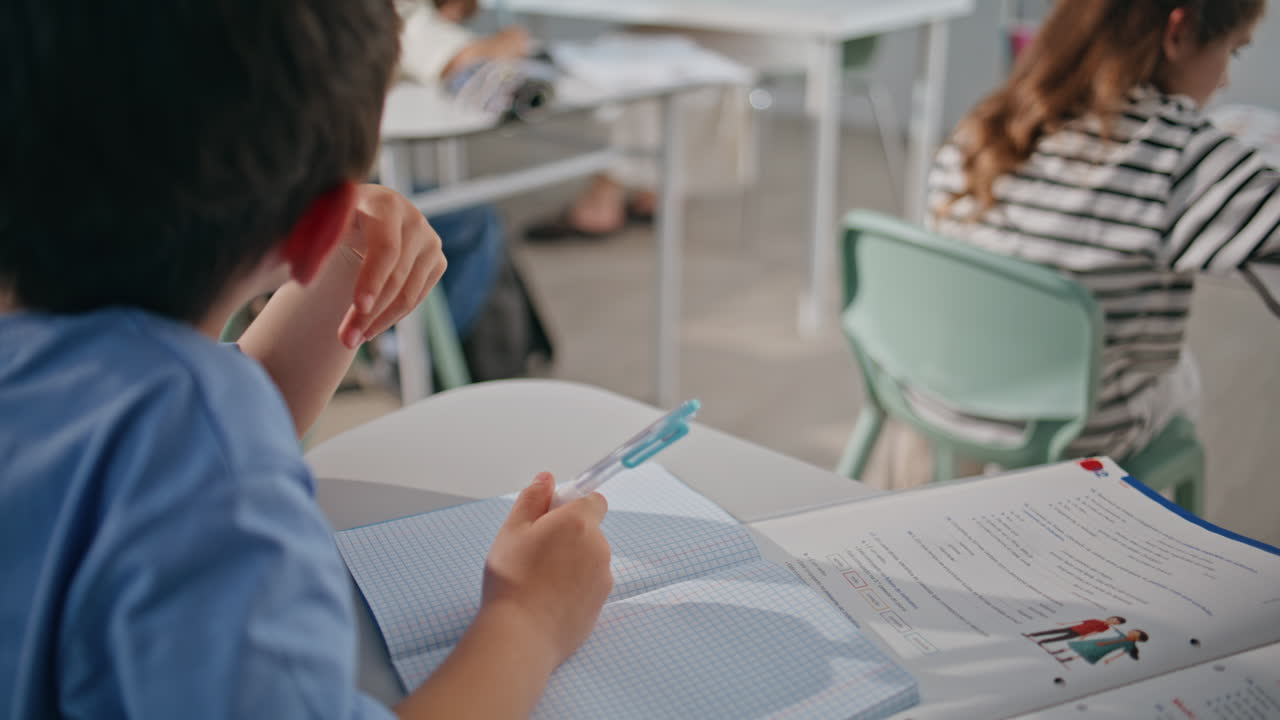 Attentive kid writing answers holding pen in classroom closeup. Boy learning