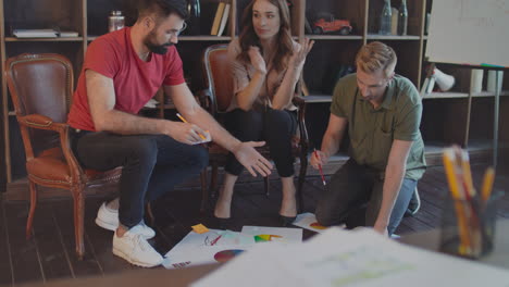 Creative-team-discussing-business-strategy-documents-on-floor-in-office