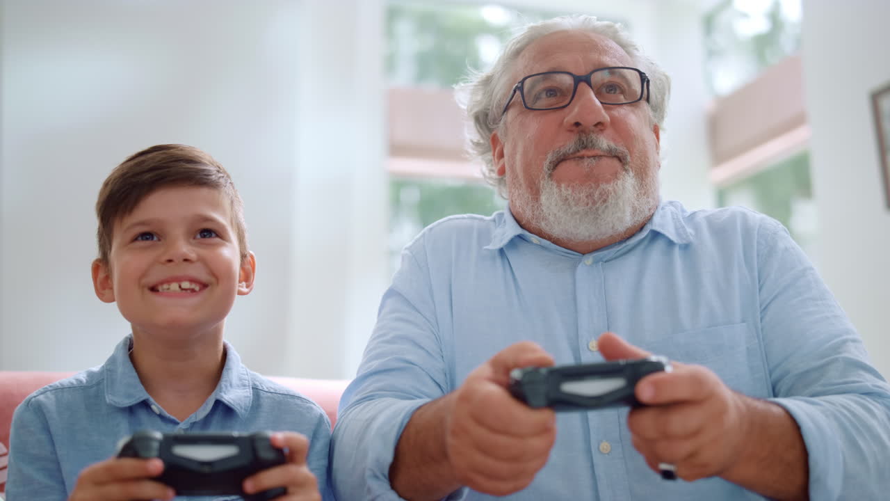 Grandfather playing video game with grandson. Mature man and boy using joysticks