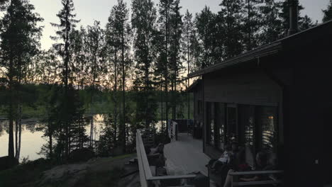 family relaxing on a cabin deck by the lake, surrounded by trees at sunset