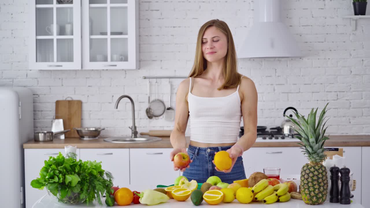 Portrait of beautiful girl in the kitchen. Vegetarian woman holding organic fruit. Happy young housewife near the table with fresh fruit and vegetables.