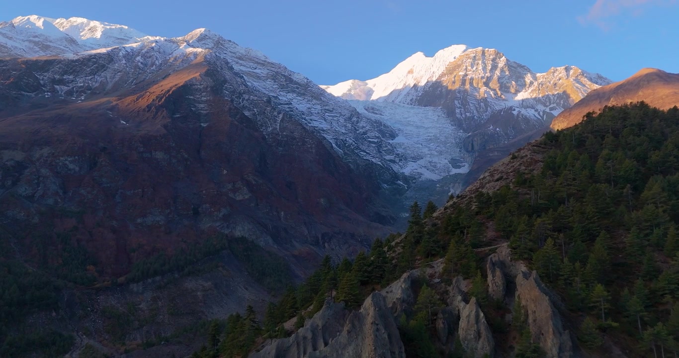 Szlak Annapurny, region Manang, Nepal, ujęcie z lotu ptaka nad surowymi zboczami górskimi w kierunku oświetlonego słońcem szczytu Gangapurna i terenu lodowcowego