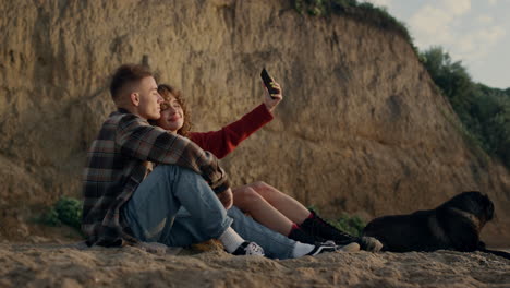 couple taking selfie photo at sunset beach on smartphone. happy lovers with dog