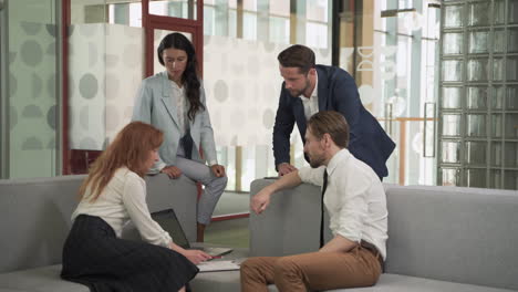 a business working group consisting of two women and two men have a relaxed meeting in the armchairs in the common area of the offices