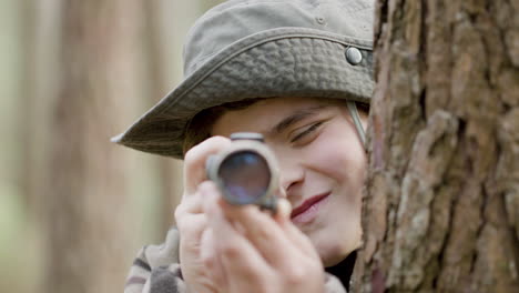 caucasian woman and boy standing between trees in the forest, observing wildlife with monocular and taking photos with professional camera