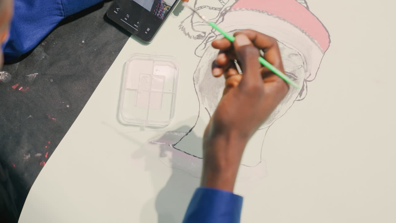 Black community artist drafting memorial painting portrait on paper, careful hand tracing tribute features of smiling black man, planning poster layout with smartphone reference, reverent atmosphere