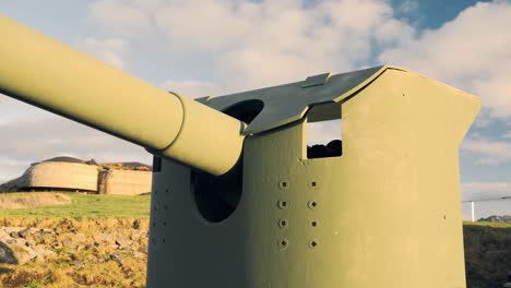 artillery cannon pointing towards the sea with a cloudy sky and a military base in the background