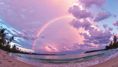 a wide-angle shot captures a serene beach at sunset with a vibrant rainbow arching across the sky