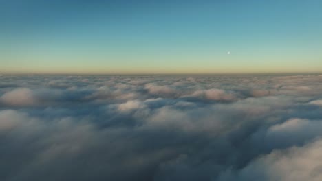 aerial view above textured clouds with a clear blue sky above and the moon just above the horizon