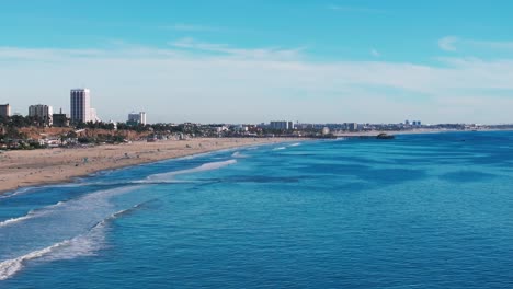 drone shot flying over santa monica beach with large waves and busy beach