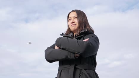 young attractive woman in winter jacket stands outside and crosses her arms