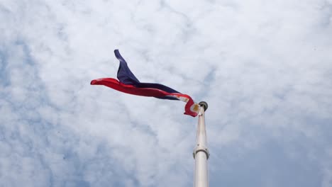 flag flying to the left as birds fly above it and cotton-like clouds as the background as captured from under the philippine national flagpole