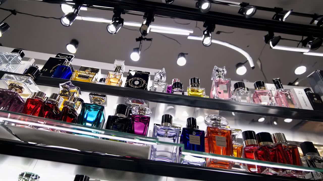 Low-angle video shot of a store shelf displaying colorful perfume bottles under bright spotlights