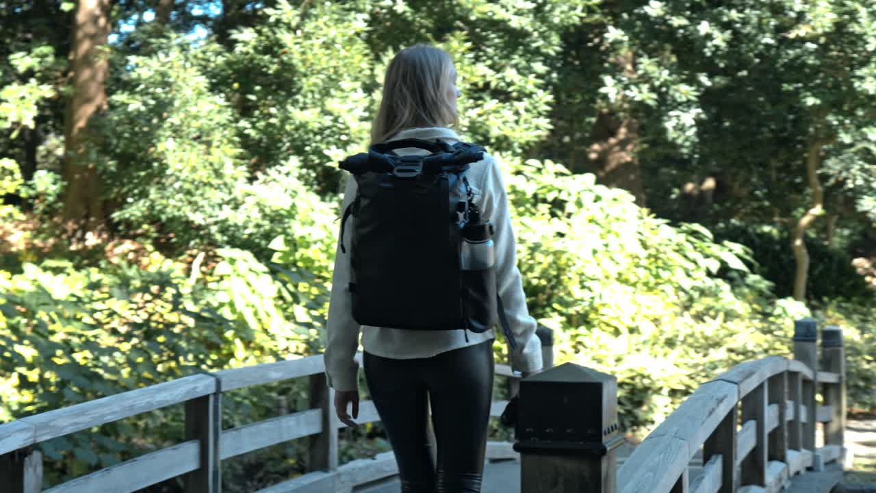 A photographer with a camera crosses a scenic bridge in the tranquil Hamarikyu Gardens, Tokyo.