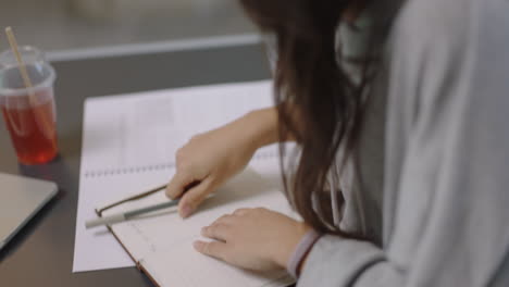 joven mujer de negocios asiática escribiendo notas disfrutando del estudio escuchando música usando auriculares estudiante bebiendo jugo en el lugar de trabajo de la oficina de cerca