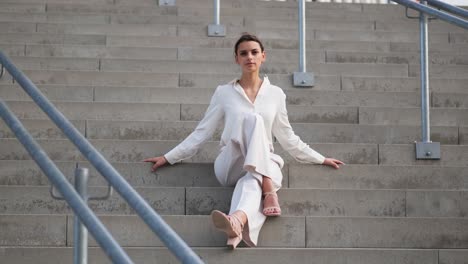 A-young-beautiful-model-sits-on-steps-in-a-beige-business-dress