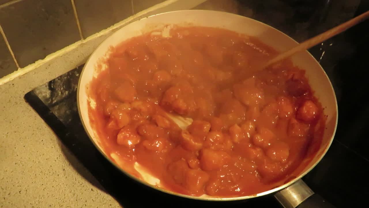 Slow motion stirring of tomato red sauce with chicken shimmering in frying pan