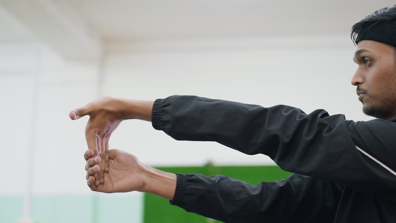 Young athlete practicing wrist flexibility during indoor training session focusing on strength, mobility, and preparation for sports activity with concentration and control in workout environment