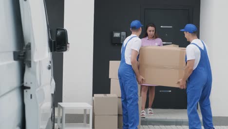 two young workers of removal company unload boxes and furniture from minibus into customer's home