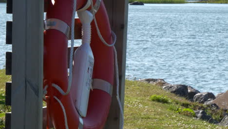 Slomo-pan-of-red-ring-lifebuoy-in-foreground-of-grass-and-wavy-sea