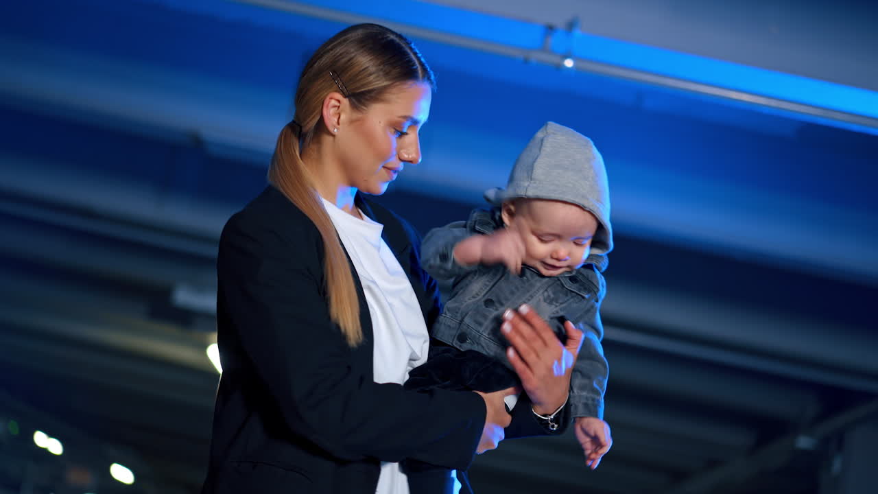 Beautiful Caucasian woman holding an infant baby in hands. Mother puts her baby down and supports him posing in front of camera.