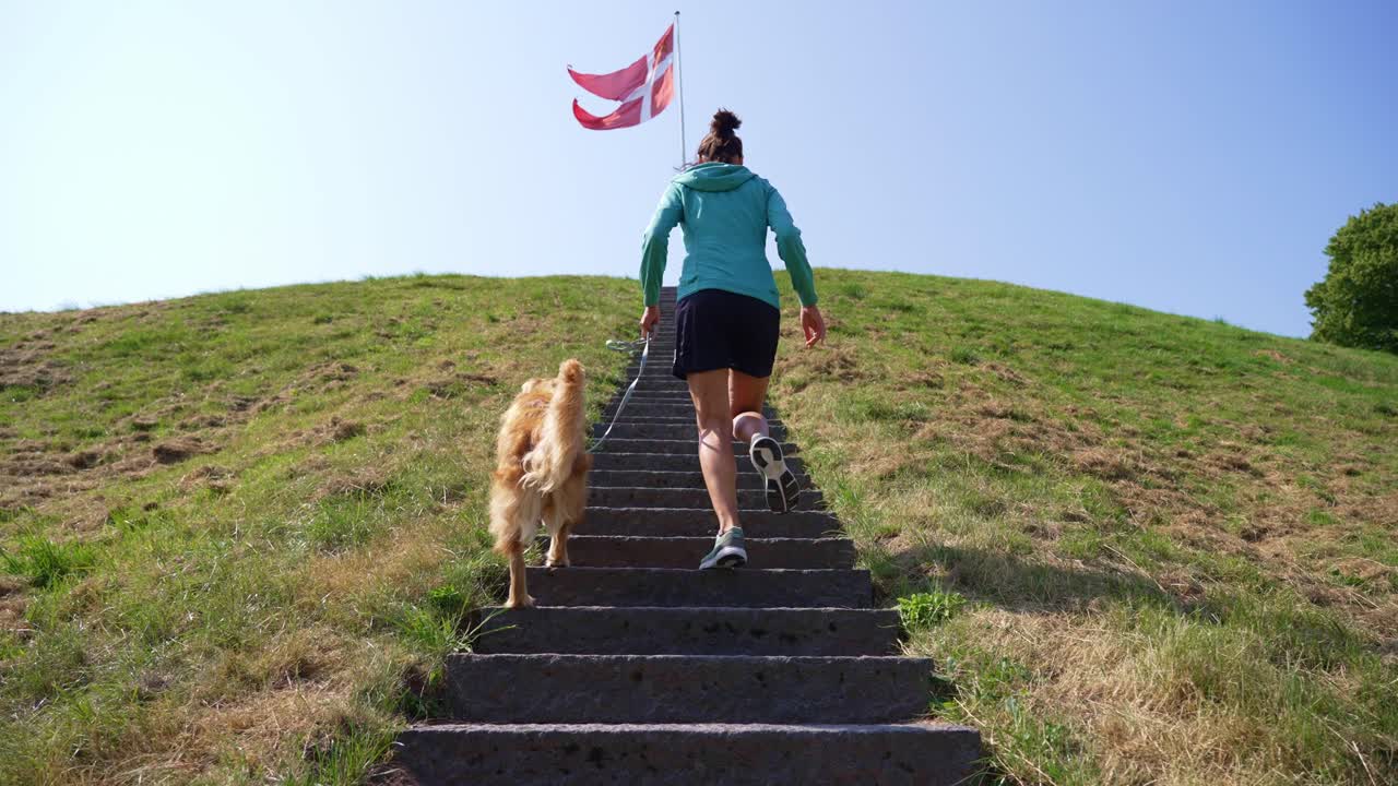 A woman and her dog walk up stairs with a Danish flag fluttering in the background