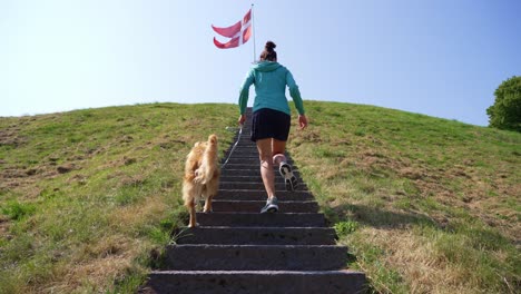 a woman and her dog walk up stairs with a danish flag fluttering in the background