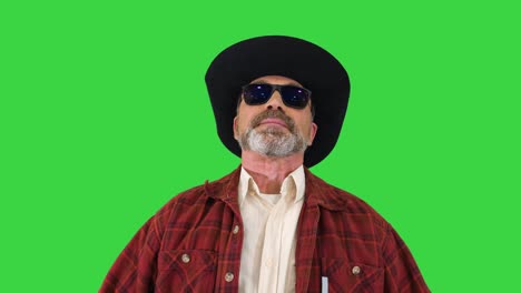 ranger in a cowboy hat putting on sunglasses and smiling to camera on a green screen, chroma key