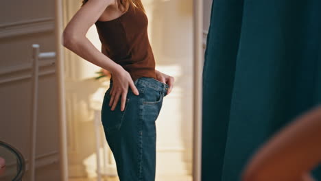 female reflection checking weight loss progress. smiling woman trying big jeans