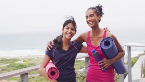 Video-of-happy-diverse-female-friends-holding-yoga-mats-and-embracing