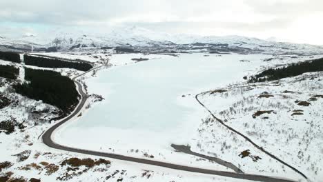 Aerial-view-descent-of-frozen-lake-and-roads,-Lofoten,-Norway---Drone-4k