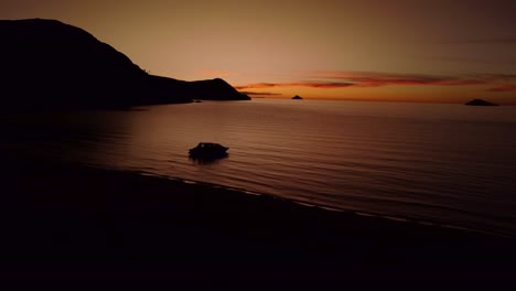 drone flying sideways on a dark orange sunset with a boat on the shore of lake titicaca in peru