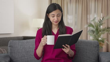 tired indian woman reading a book and drinking coffee