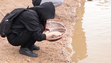 person panning for gold by the water